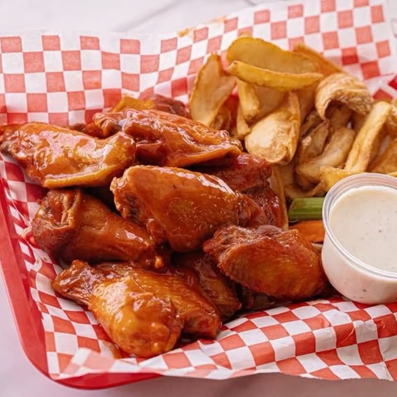 Buffalo wings with french fries, celery, carrots, and ranch dressing in a red checkered basket.