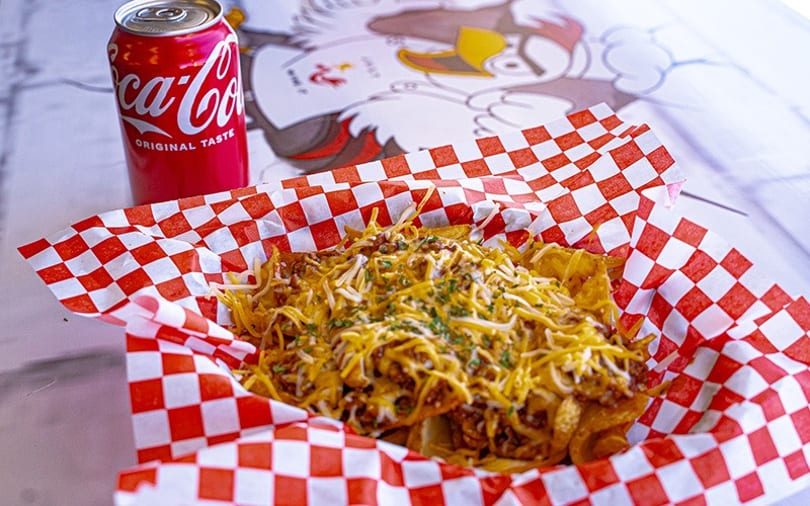 Chili cheese fries in a red and white checkered basket with a Coca-Cola can beside it.