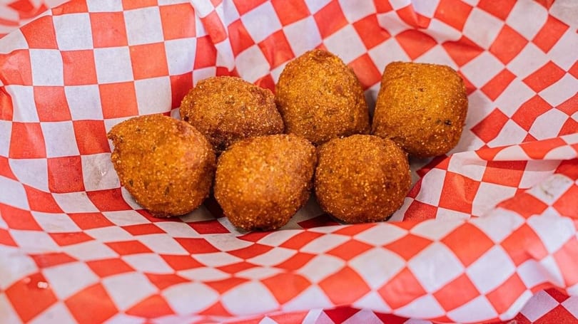Six golden-brown hush puppies rest in a red and white checkered paper-lined basket.