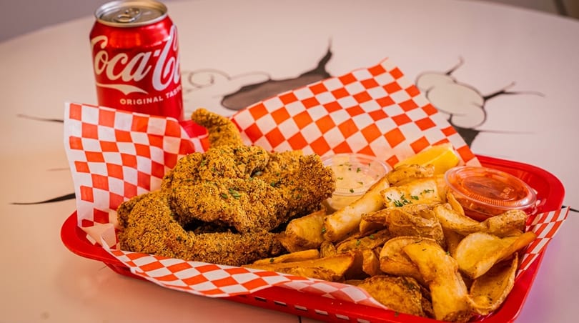 Fried fish and potato wedges in a red basket with a Coca-Cola can and dipping sauces.