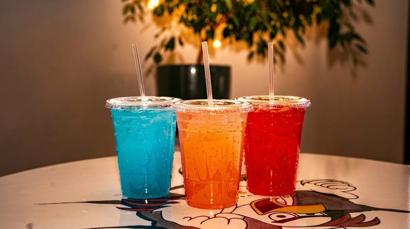 Three colorful drinks in plastic cups with straws, on a table with a cartoon design.