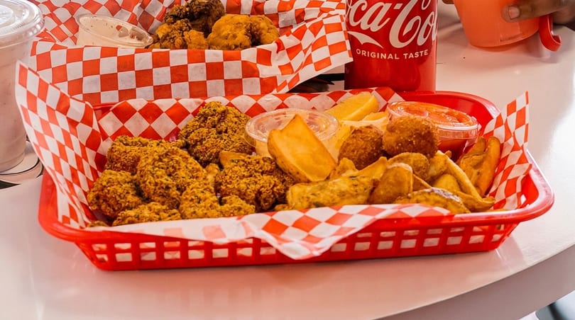 Two red baskets filled with fried chicken, potato wedges, and dipping sauces on a white table.