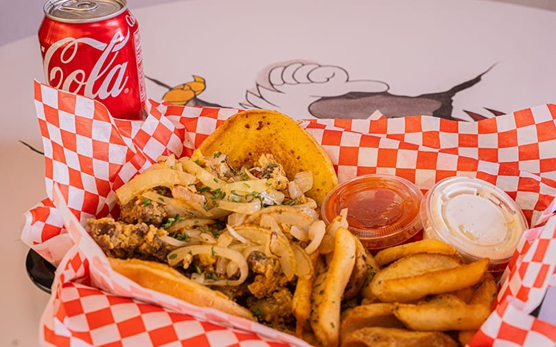 A basket of fried food with onions, fries, a golden pastry, two sauces, and a Coca-Cola can.