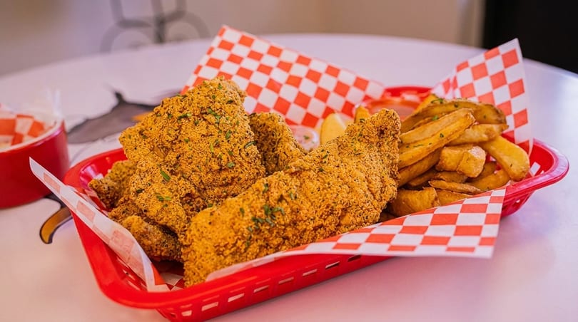 Crispy fried fish fillets and golden french fries served in a red basket with checkered paper.